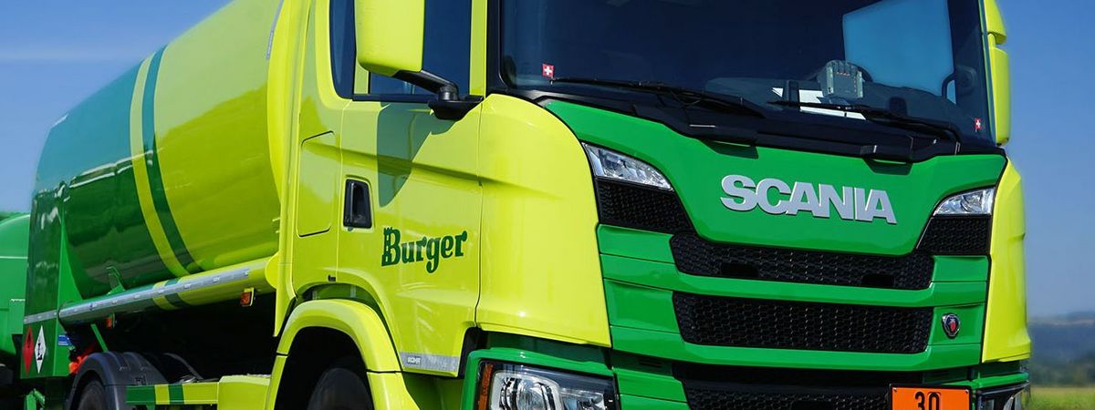 Heizöl Tankwagen in zwei Grüntönen von Burger Heizöl + Treibstoffe vor blauem Himmel und grünen Feldern.